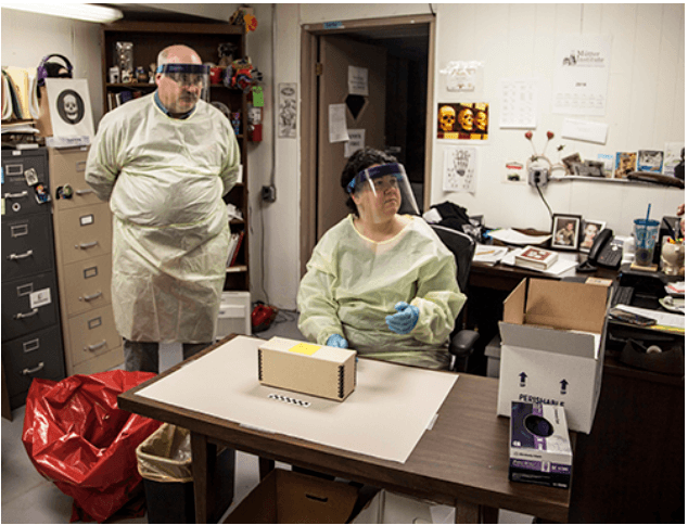 Two people in personal protective equipment looking at an item on a table.